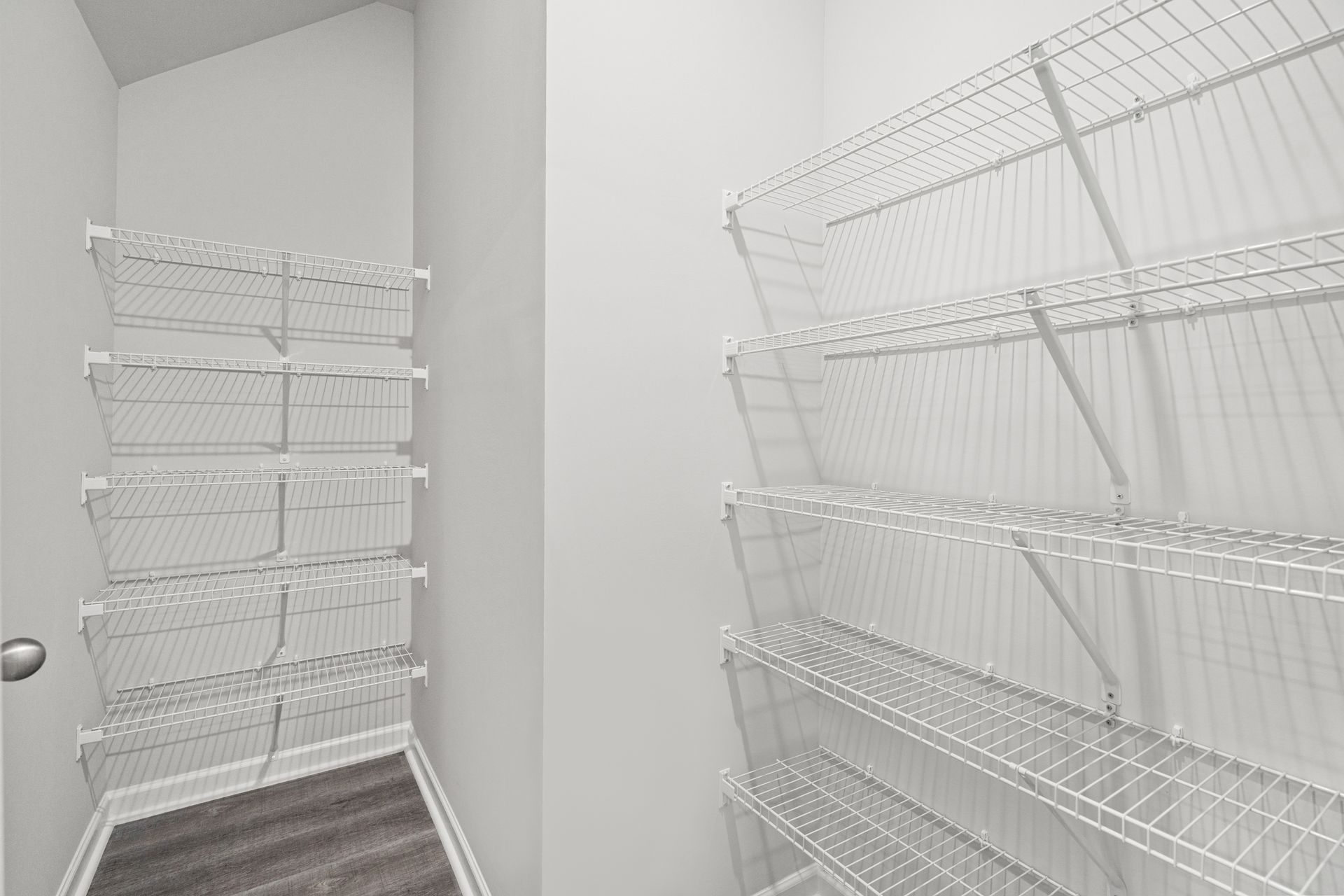 A walk in closet with white wire shelves and a wooden floor.