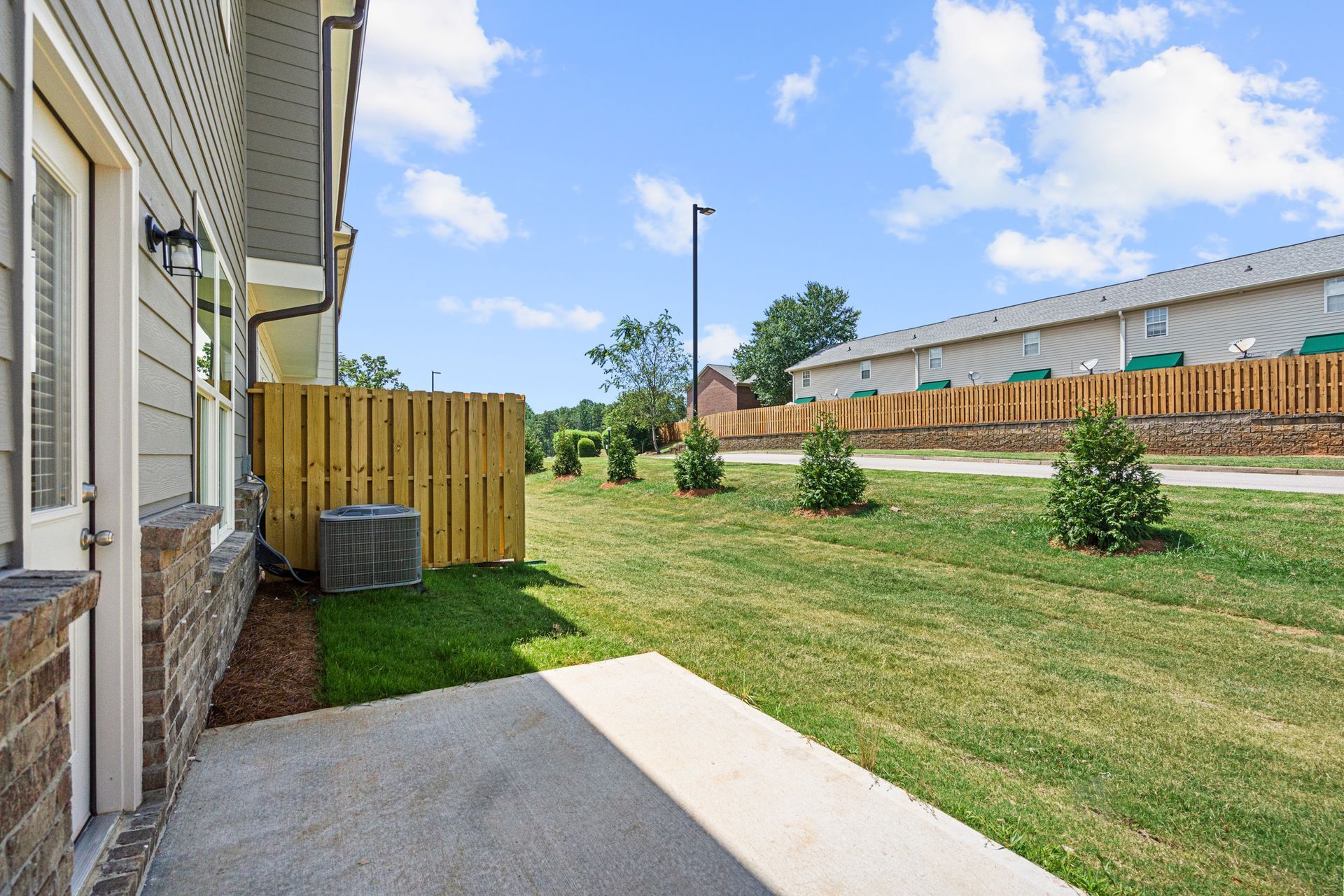 A concrete walkway leading to a house with a wooden fence in the background.