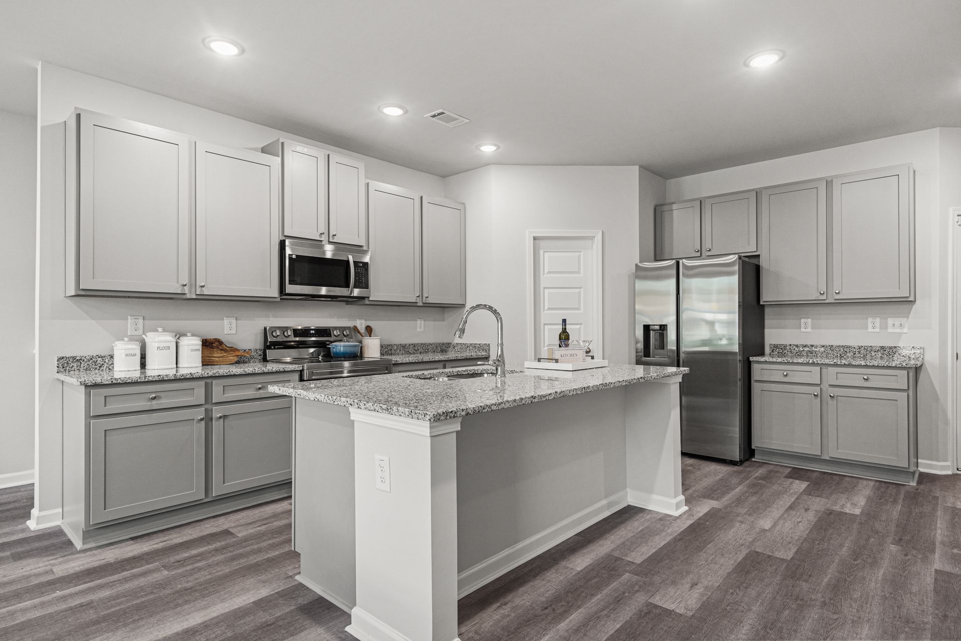 A kitchen with white cabinets , granite counter tops , stainless steel appliances and a large island.