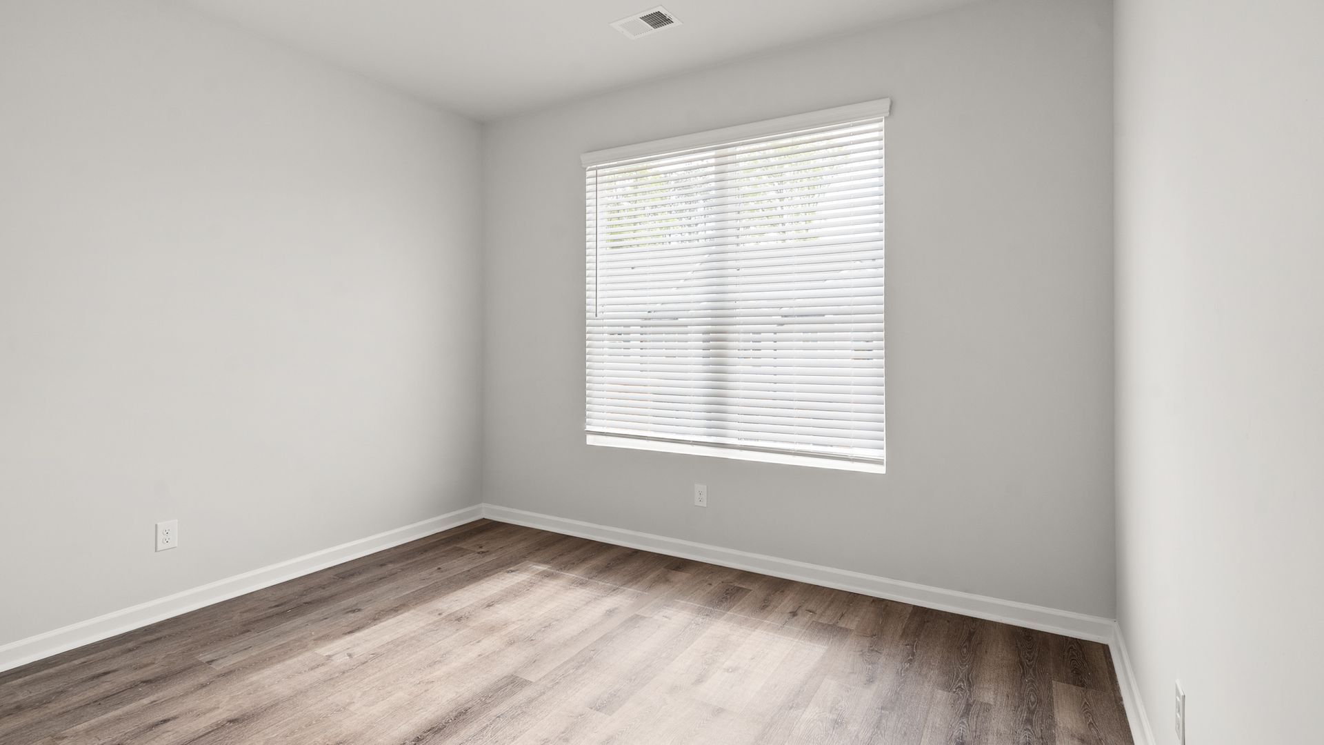 An empty room with hardwood floors and a window with blinds.