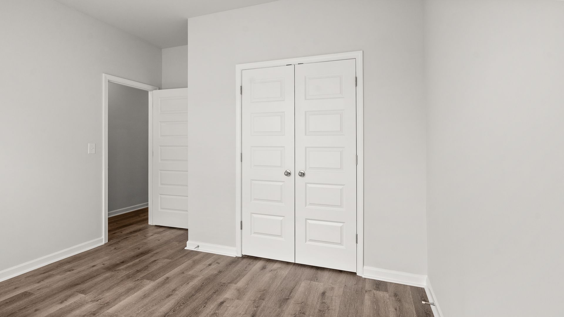 An empty bedroom with hardwood floors , white walls , and a closet.