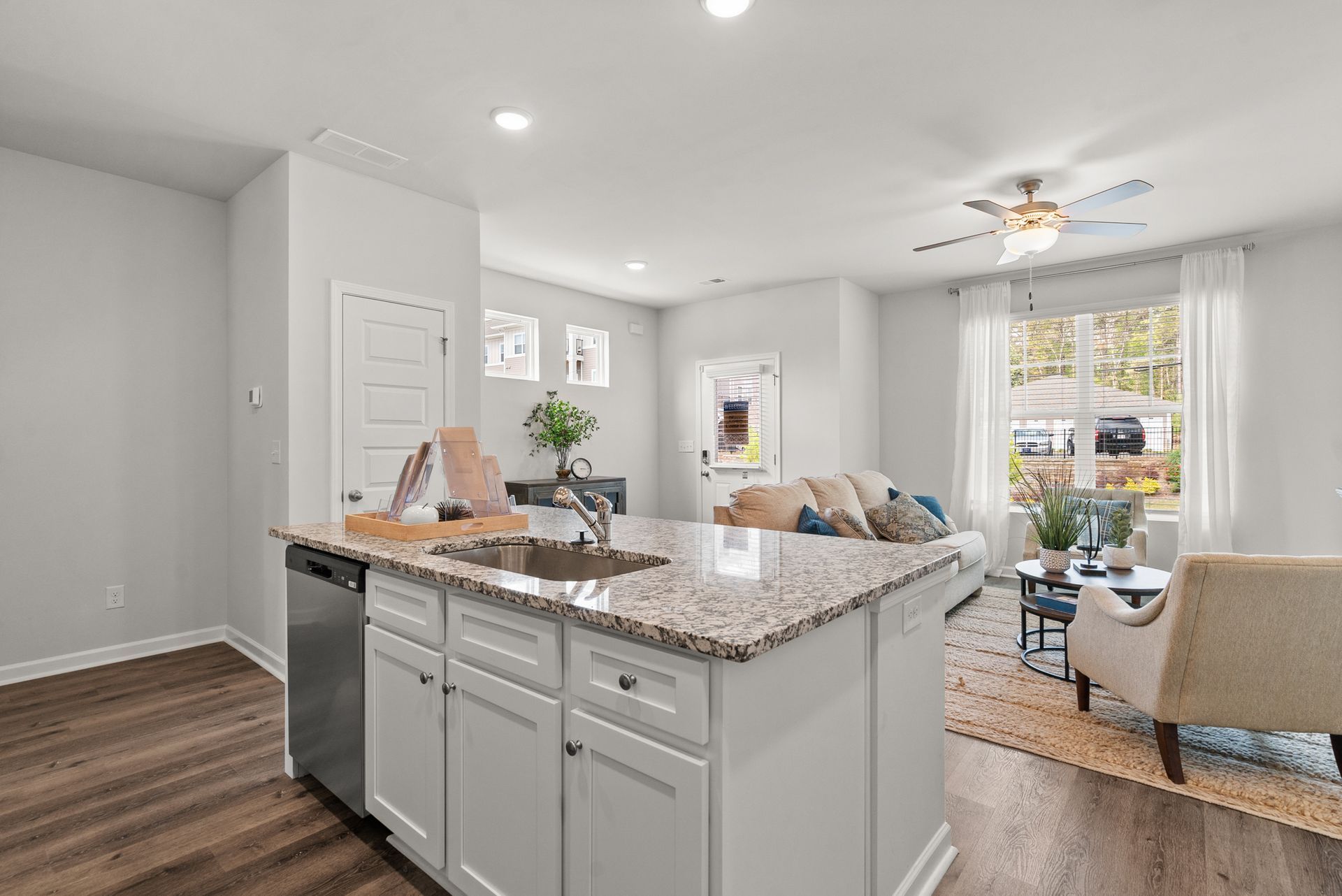 A kitchen with granite counter tops , white cabinets , a sink and a dishwasher.