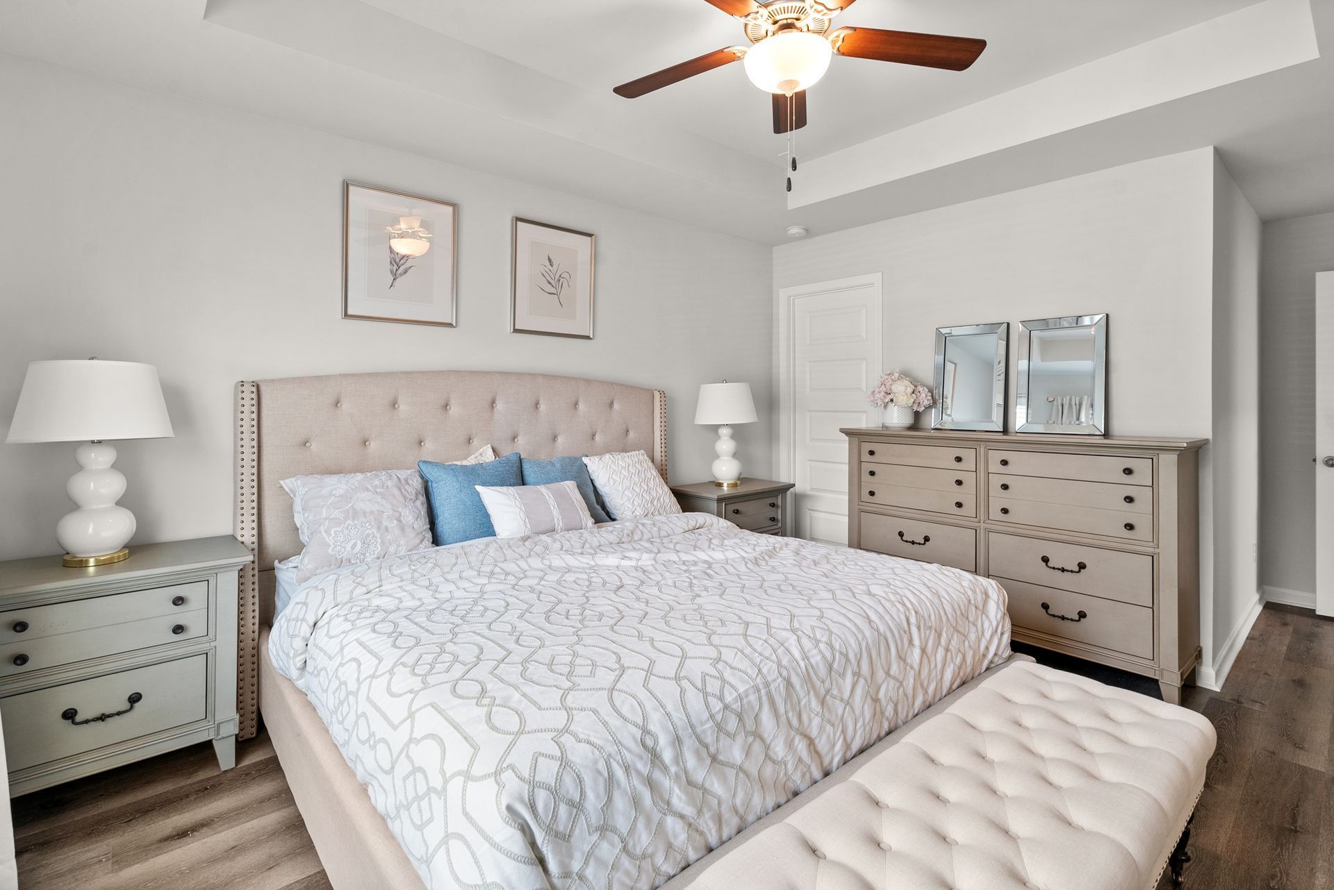 A bedroom with a bed , dresser , nightstand , lamps and a ceiling fan.