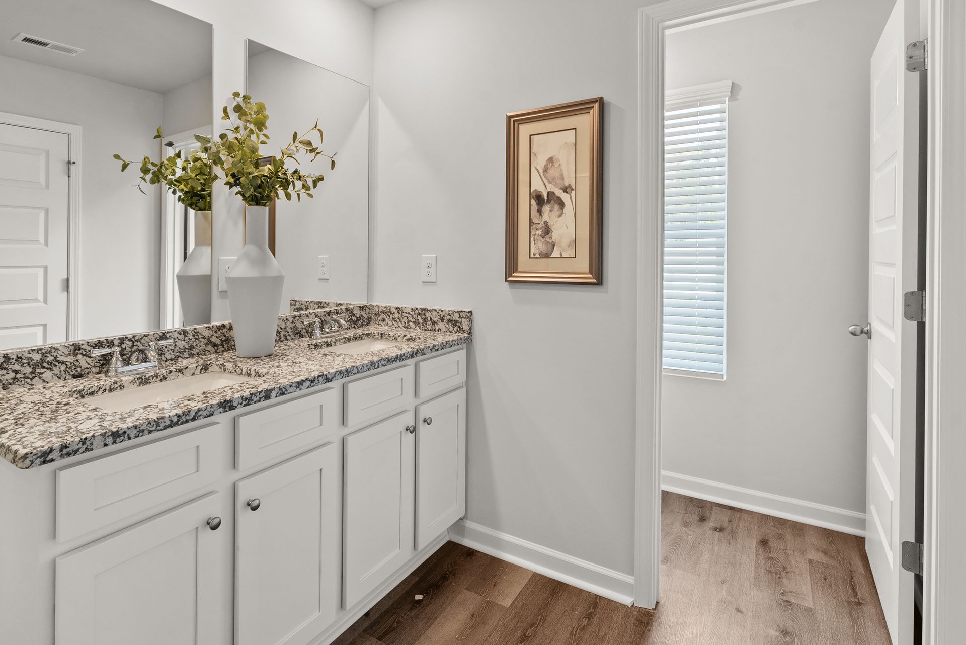 A bathroom with a sink , mirror , cabinets and hardwood floors.