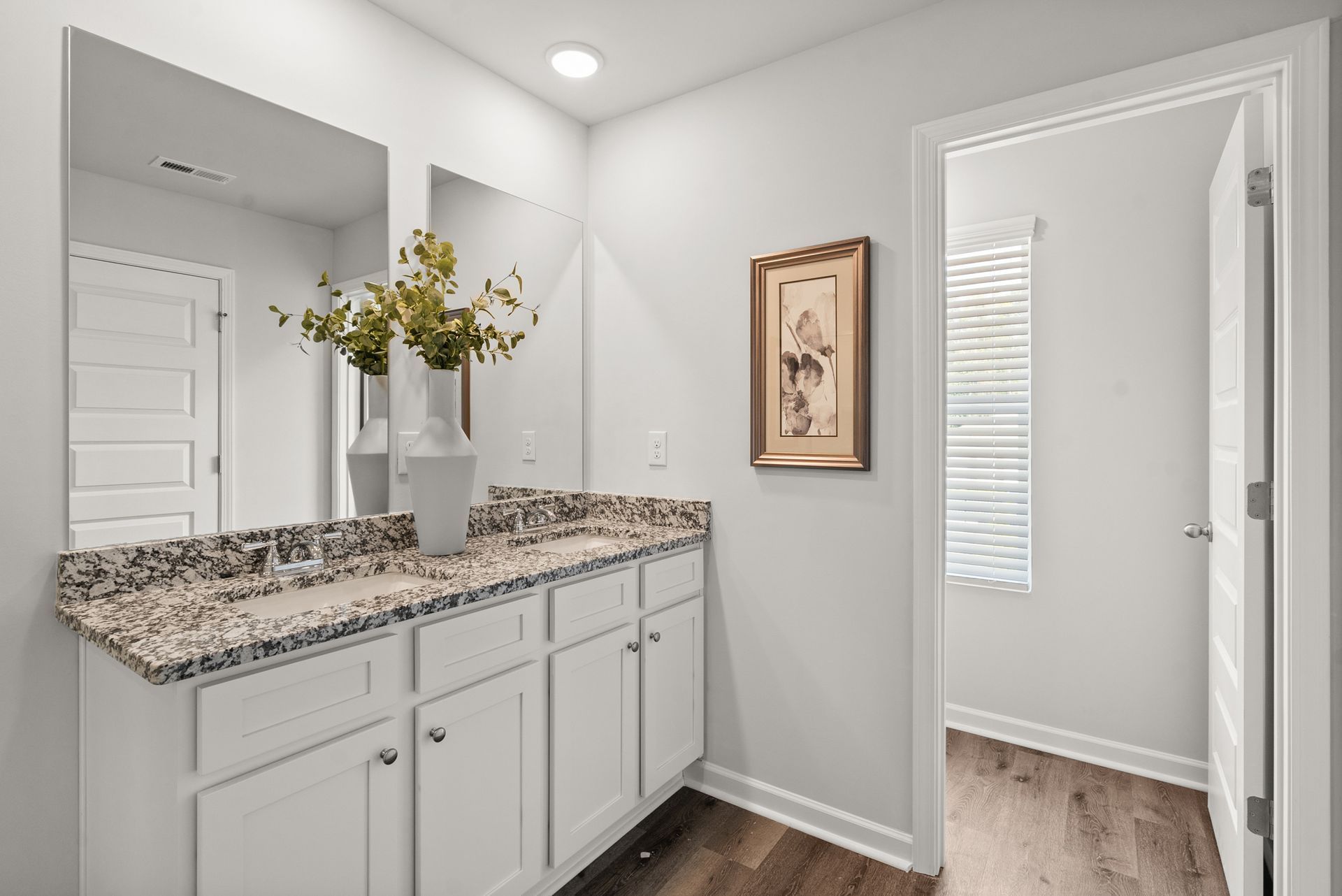 A bathroom with a sink , mirror , cabinets and hardwood floors.