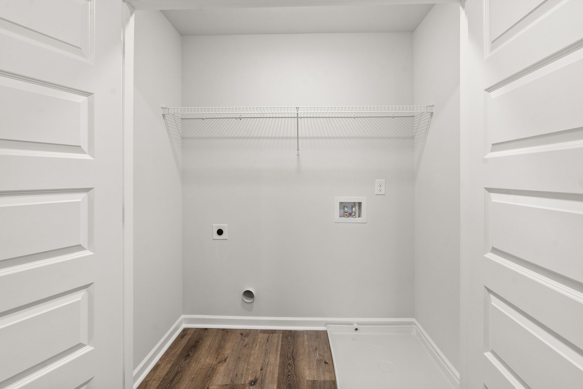 An empty laundry room with wooden floors and white walls.