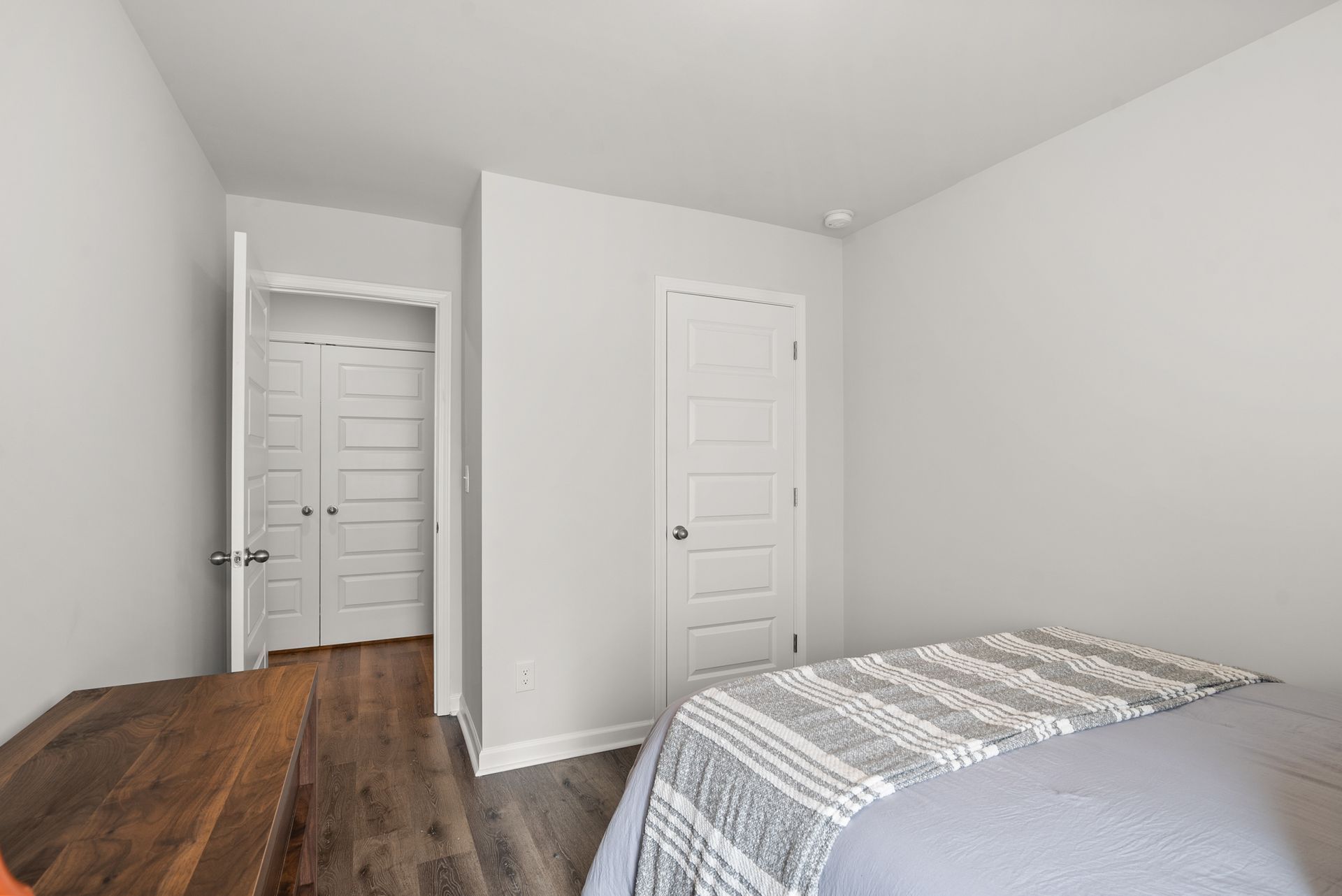 A bedroom with a bed , closet and hardwood floors.