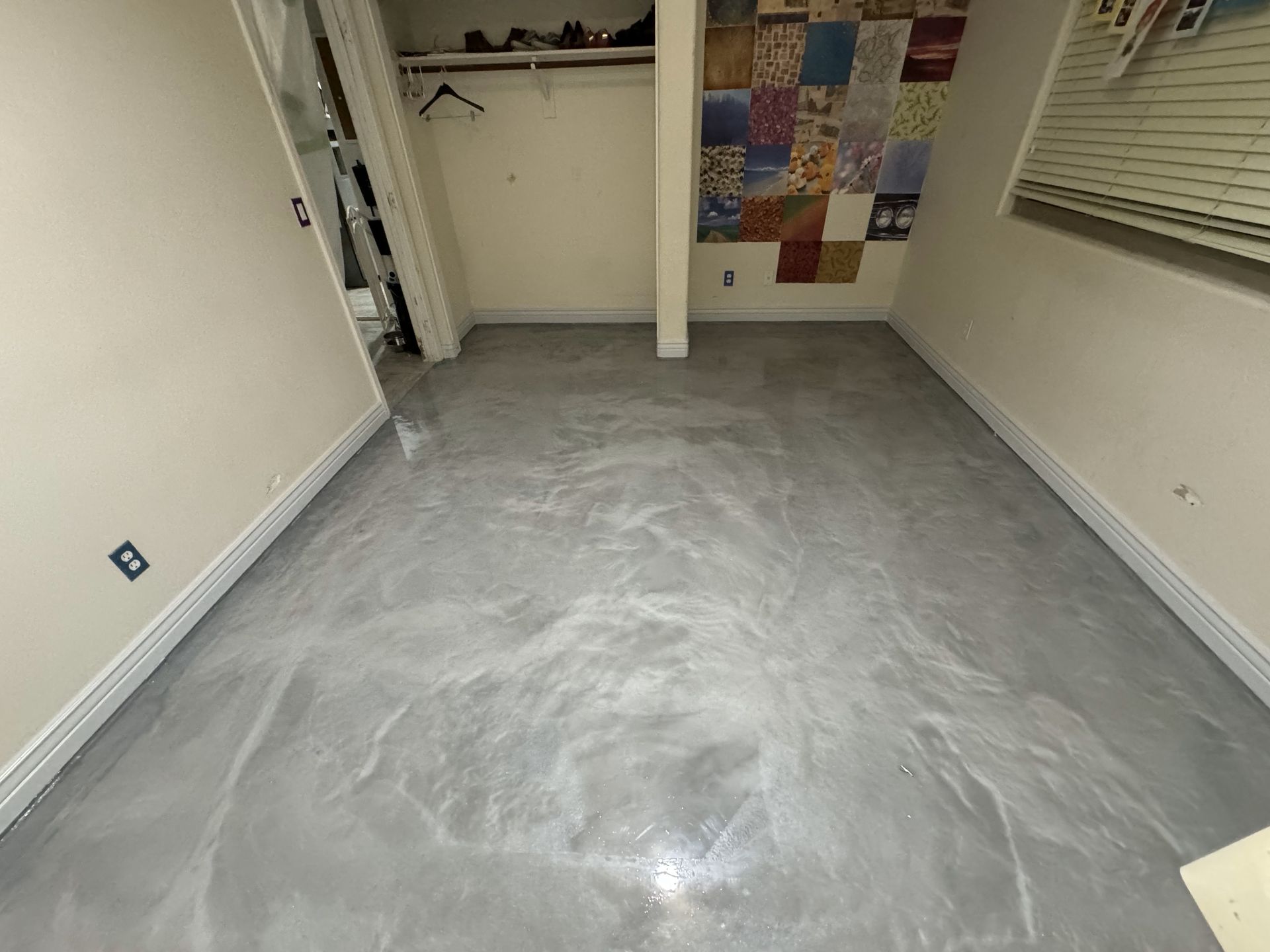 A room with a gray floor and a painting on the wall.