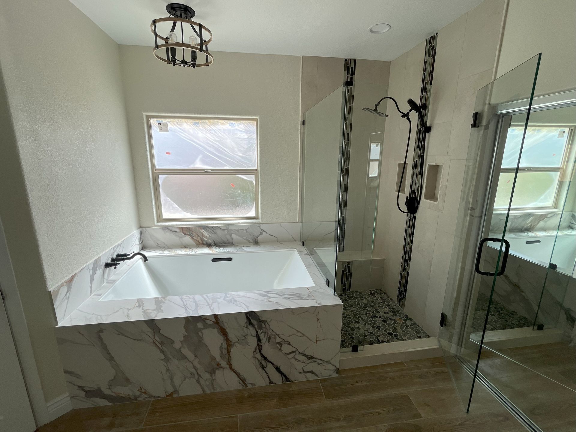 A bathroom with a tub , shower , mirror and window.