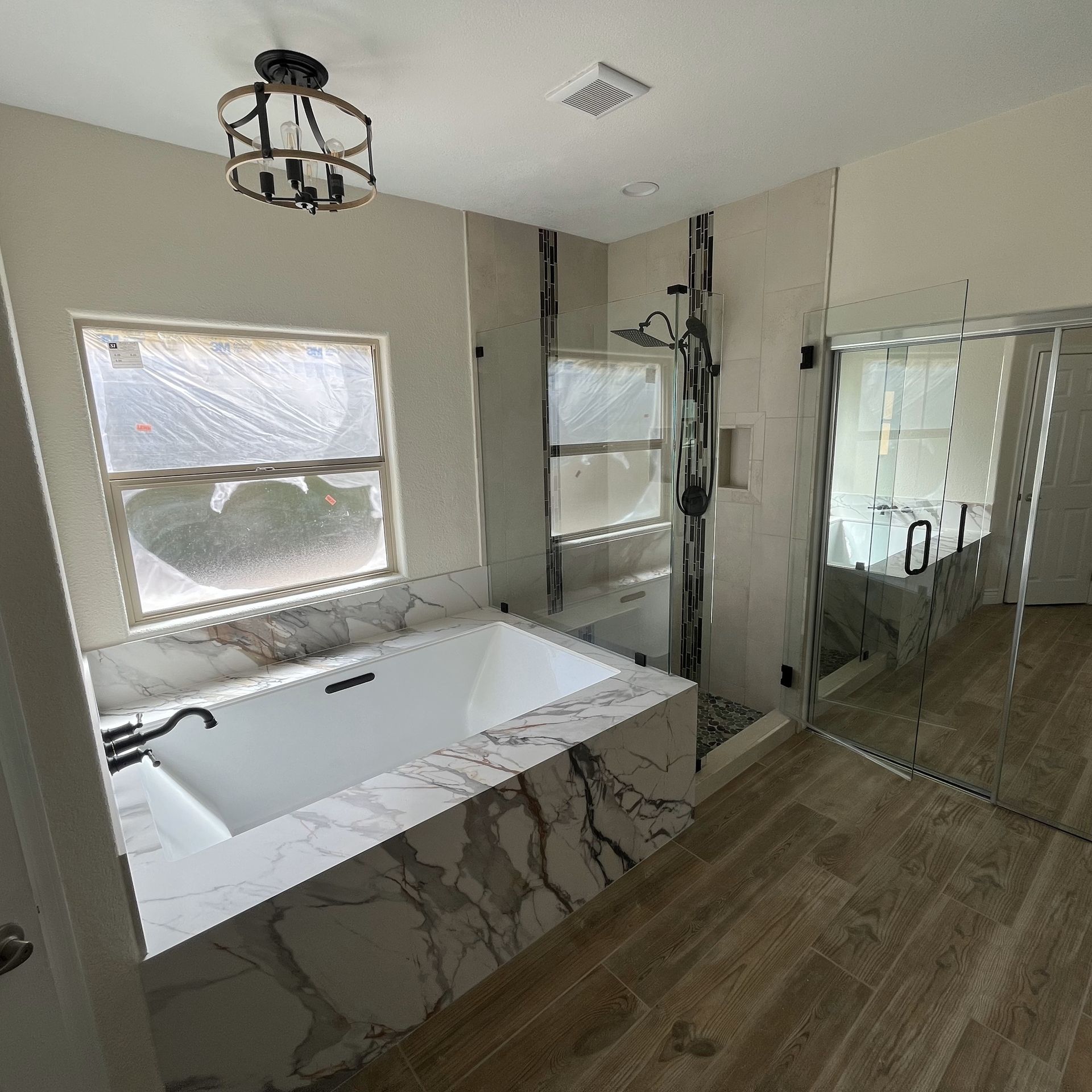 A bathroom with a tub , sink , mirror and window.