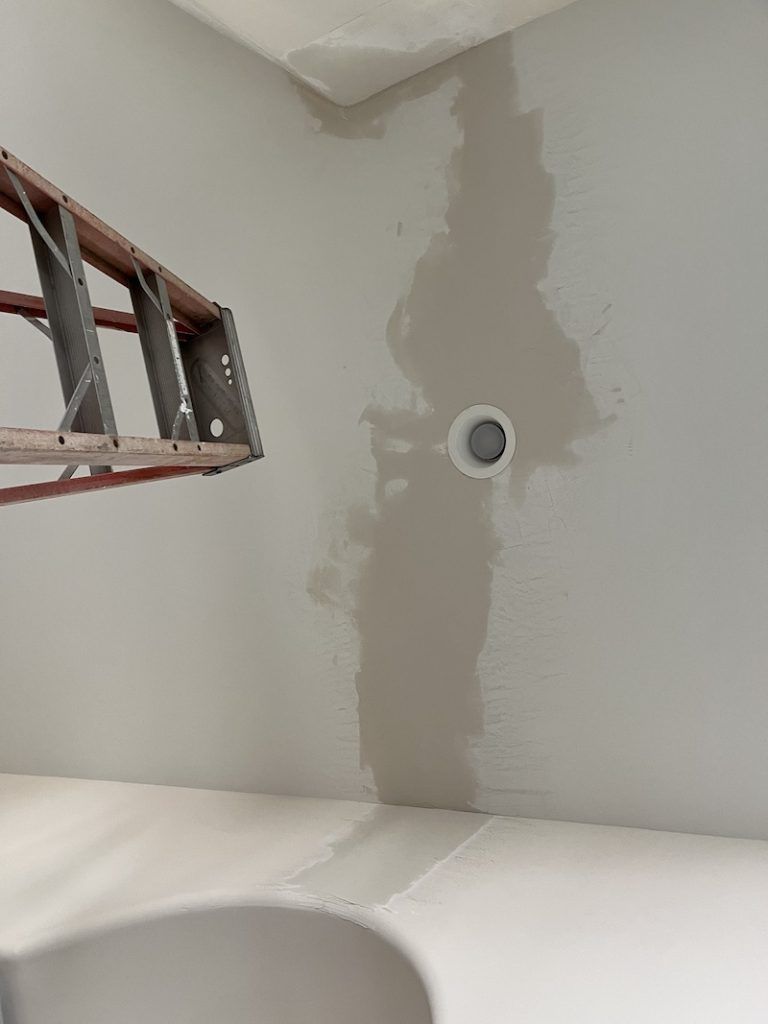 A ladder is hanging from the ceiling next to a hole in the wall.