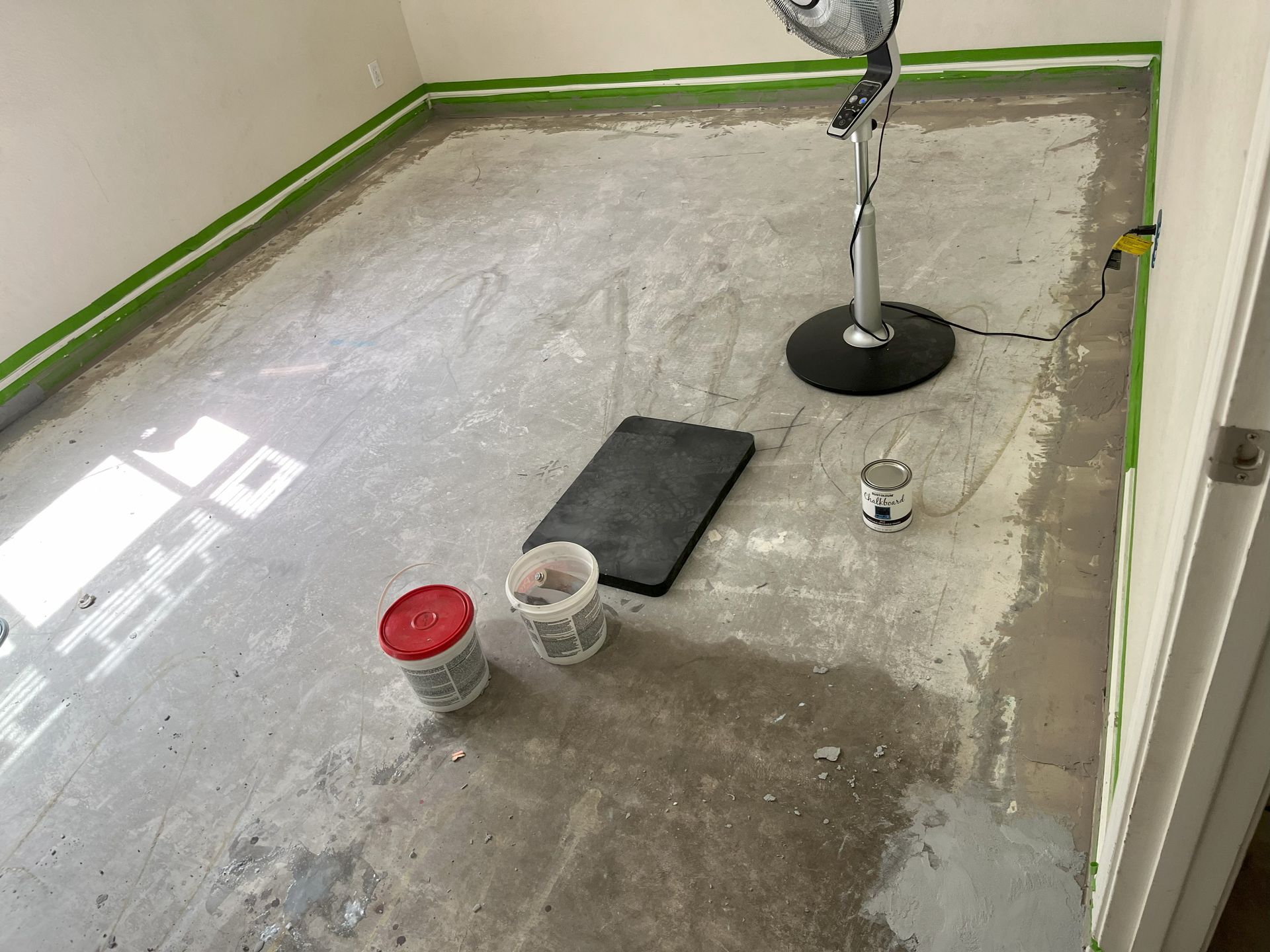 A room with a fan and buckets of paint on the floor.