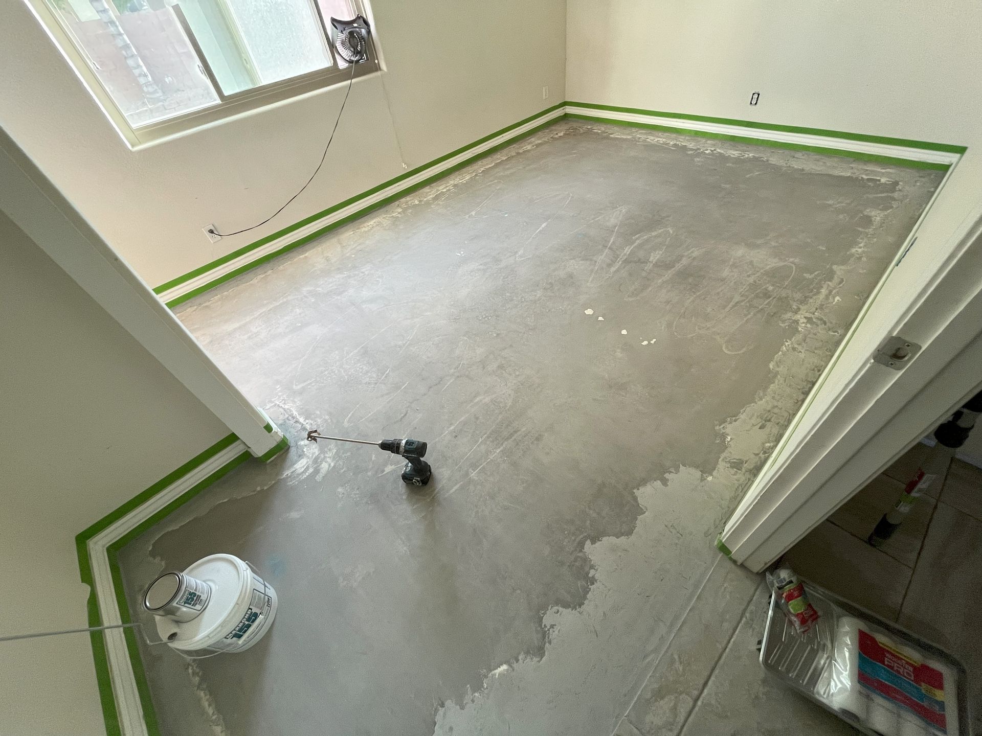A room with a concrete floor and a drill on the floor.