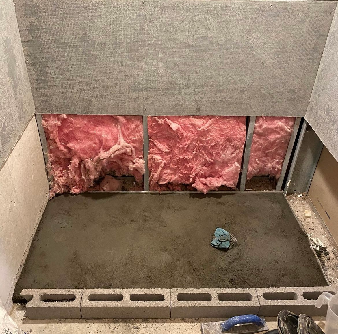 A concrete floor is being built in a room with pink insulation.