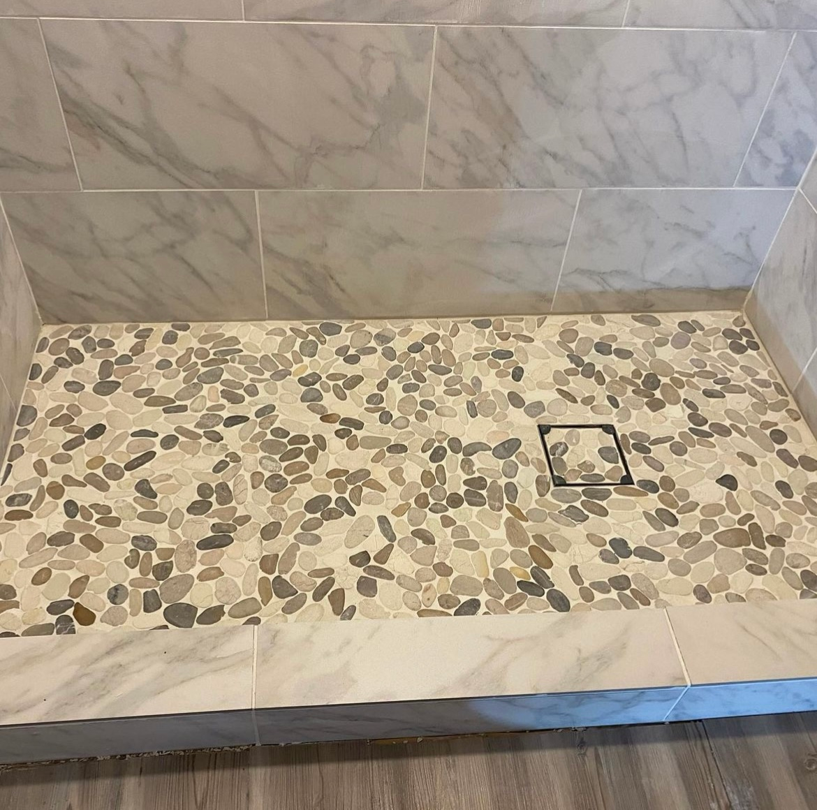 A walk in shower with a tiled floor and a drain.