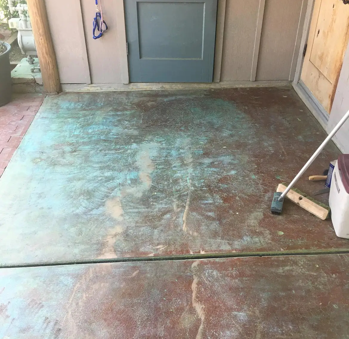 A mop is sitting on a dirty concrete floor in front of a door.