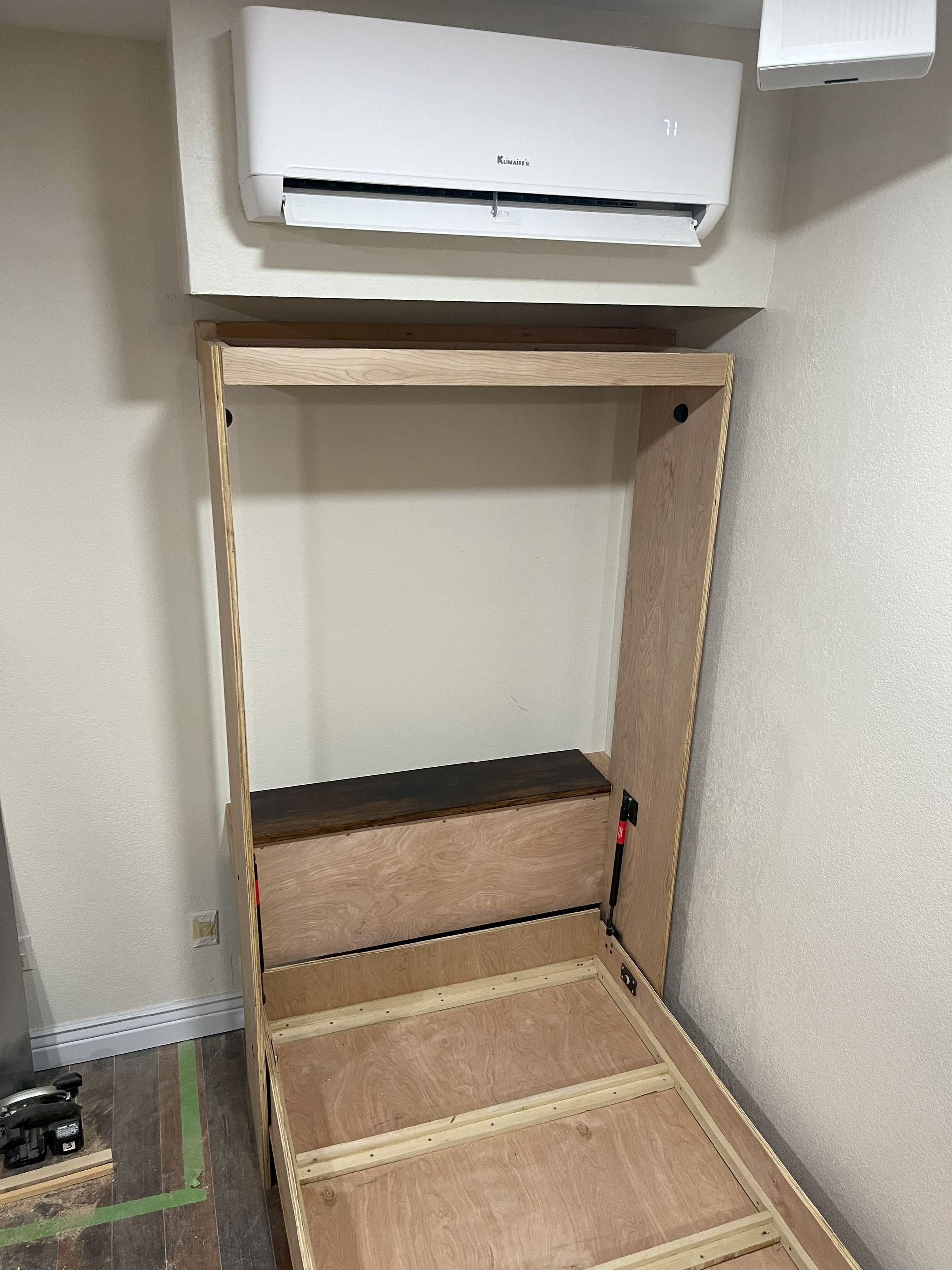 A bed is being built in a room with a wall mounted air conditioner.