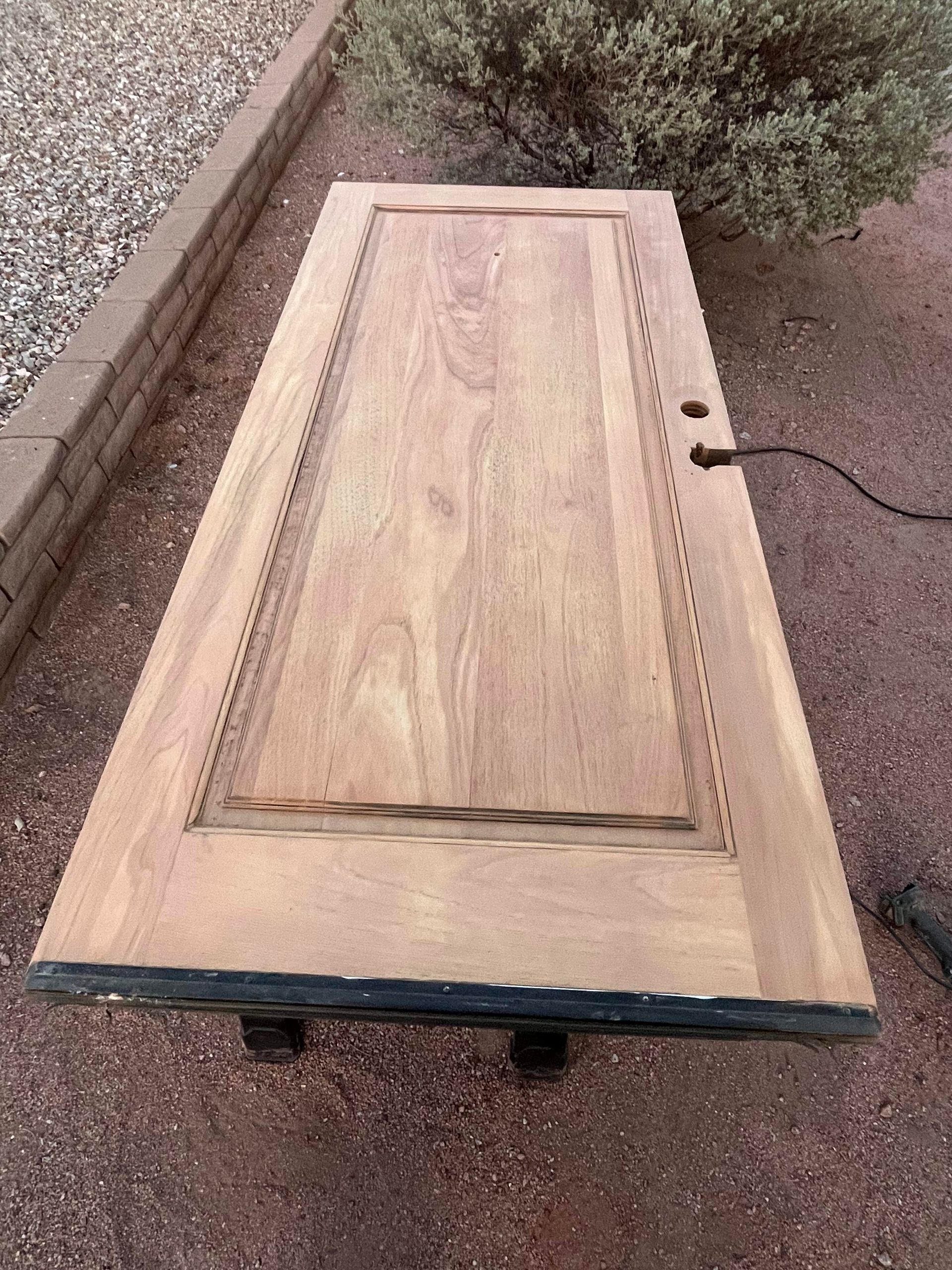 A wooden door is sitting on the ground next to a bush.