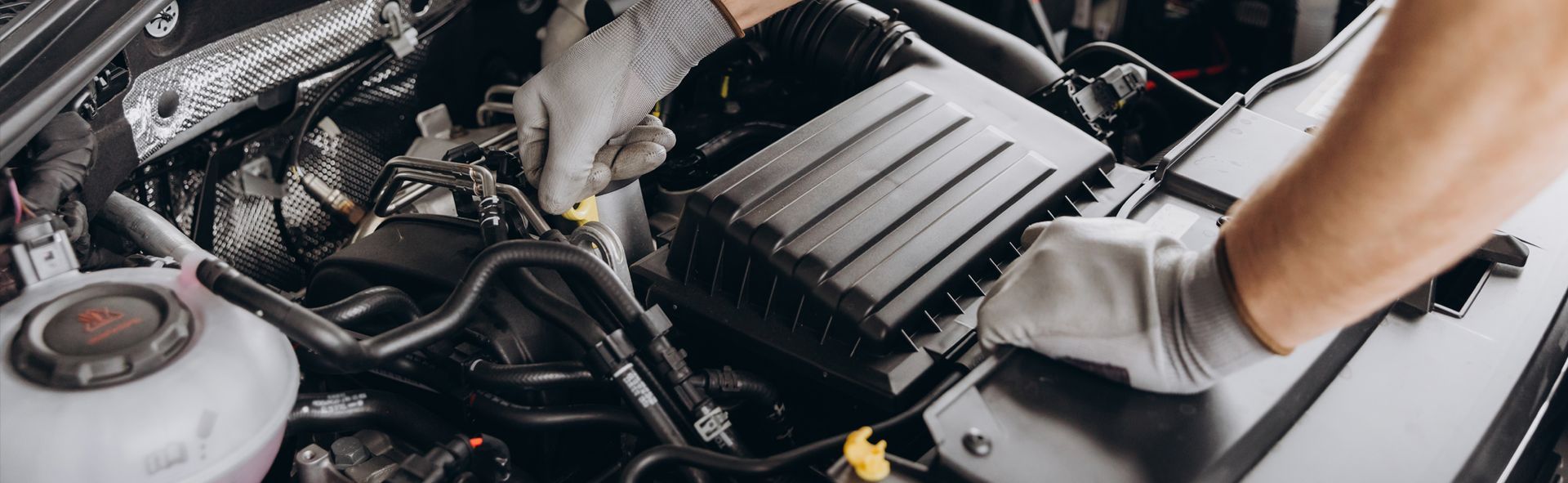 A mechanic wearing gloves works on a car engine, possibly for repair or maintenance.