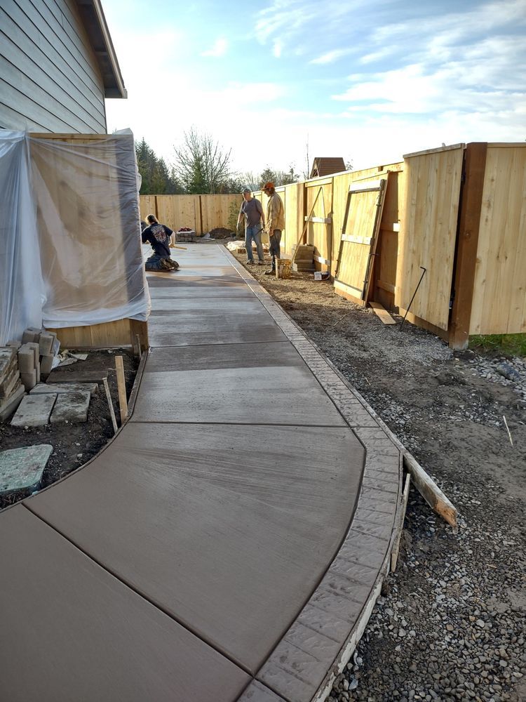 A concrete walkway is being built in a backyard next to a wooden fence.