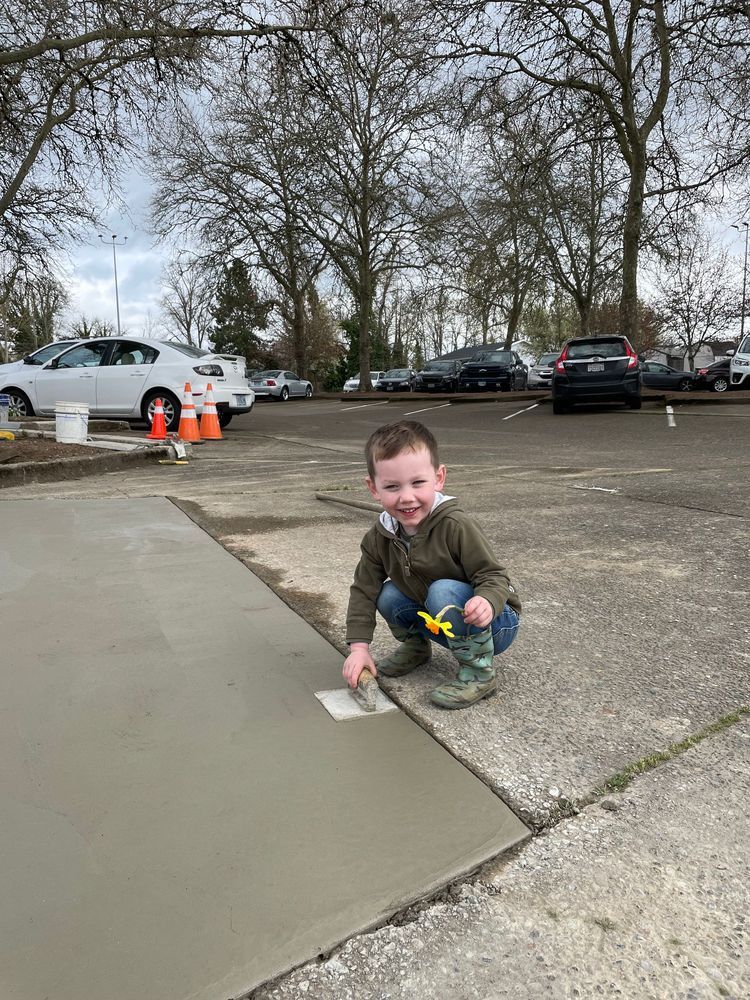 A young boy is kneeling down on a sidewalk with a trowel.