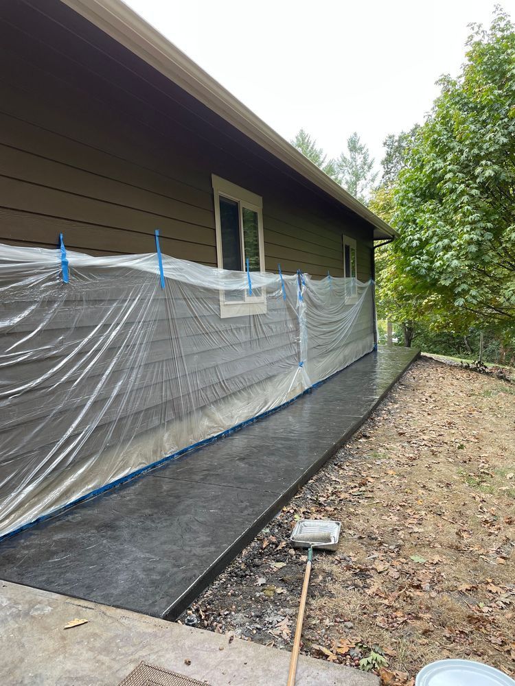 A house is covered in plastic while a sidewalk is being painted.