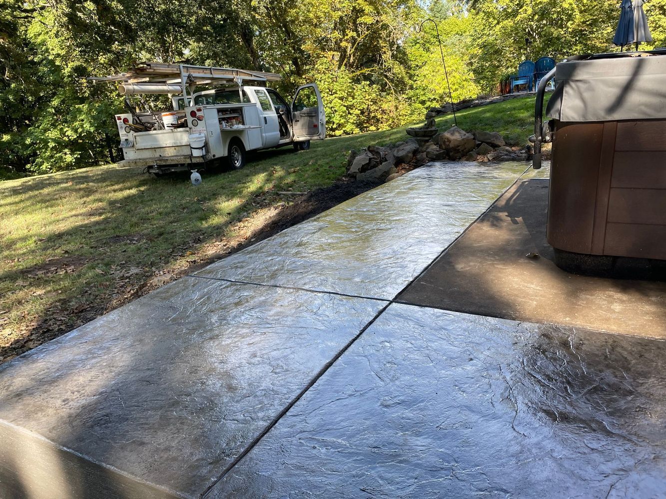 A truck is parked on the side of a concrete driveway next to a hot tub.
