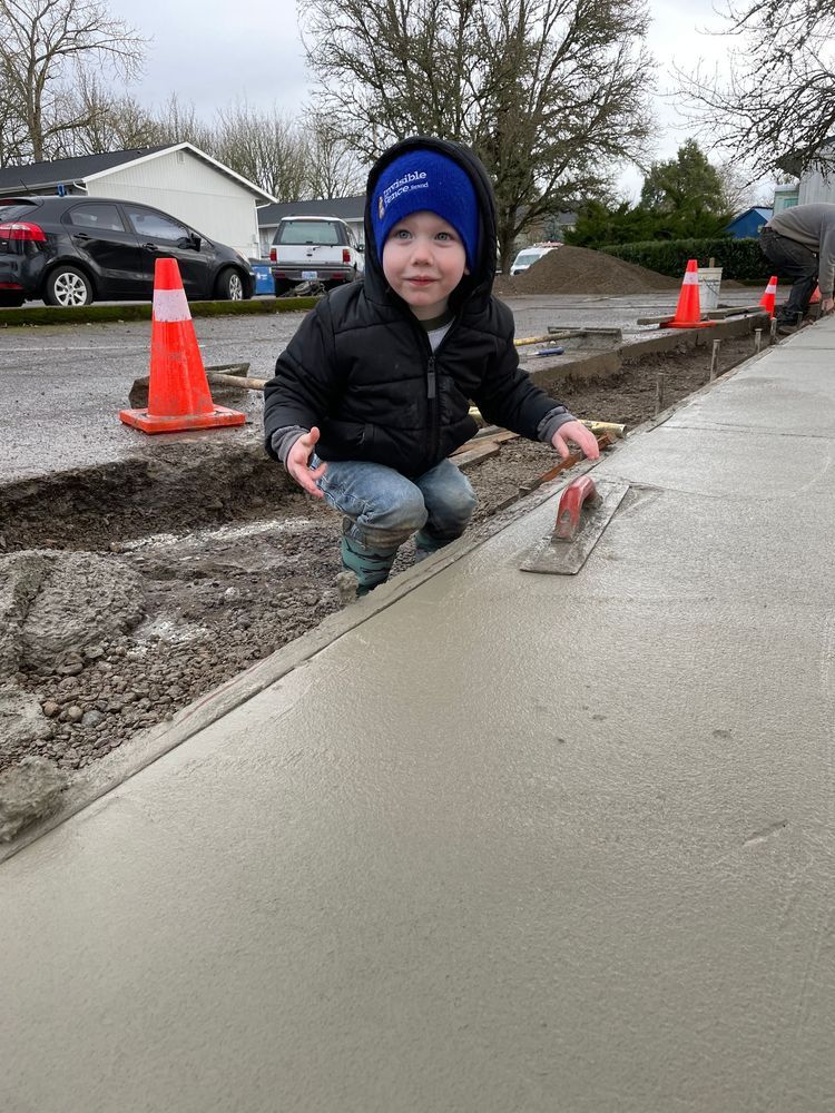 A little boy is kneeling down on a sidewalk with a trowel.