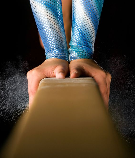 A close up of a gymnast performing a routine on a balance beam.