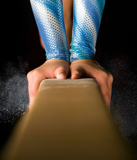 A close up of a gymnast performing a routine on a balance beam.