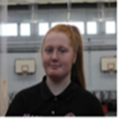 A woman in an orange shirt is smiling and wearing a necklace.