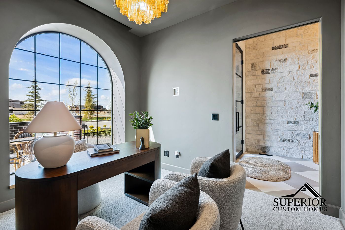 A living room with a desk , chairs , and a large window.