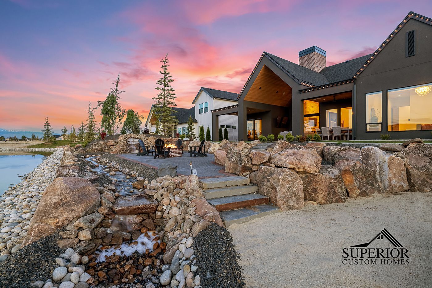 A large house is sitting on top of a rocky hill next to a body of water.