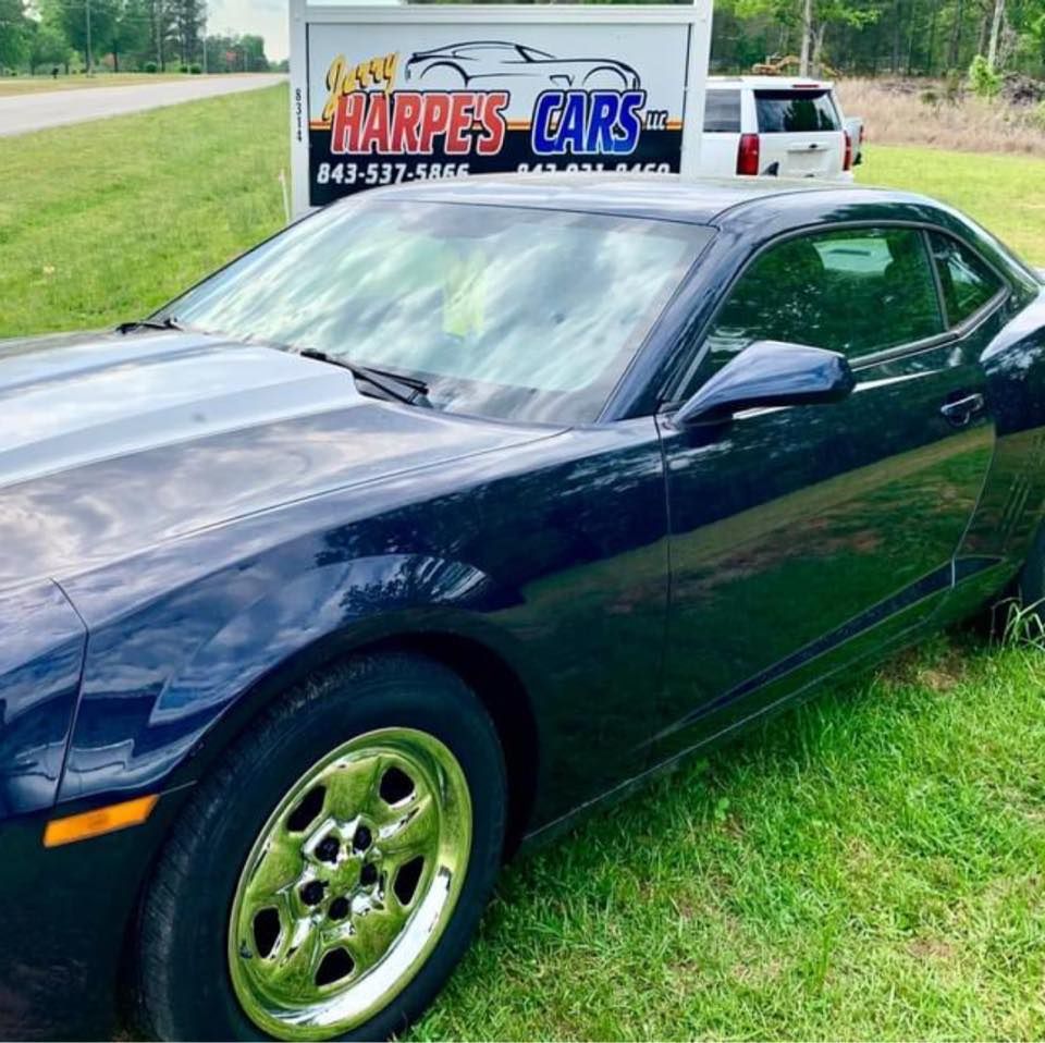 A blue car is parked in front of a harpes cars sign