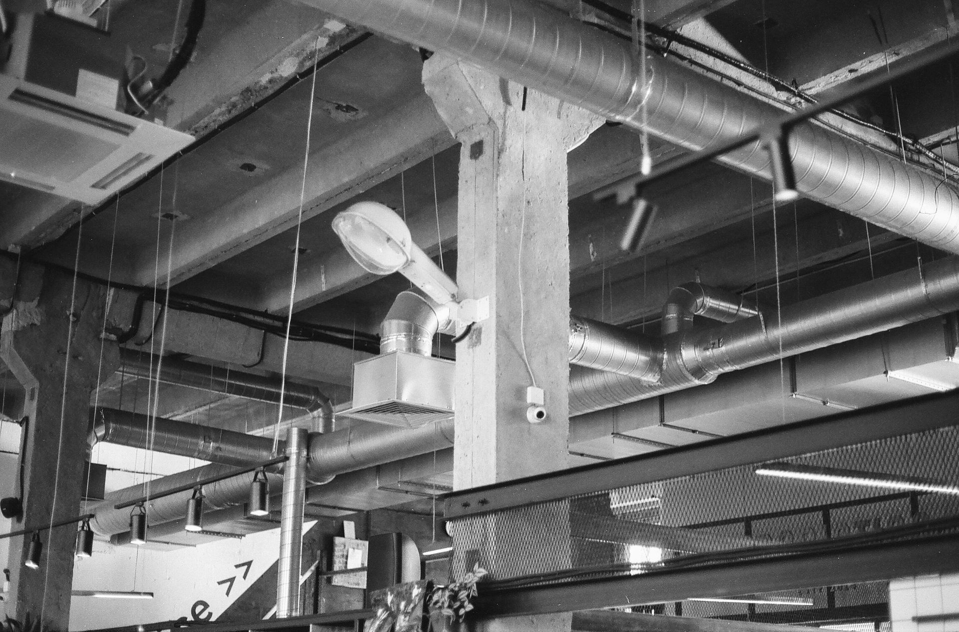 Exposed ceiling of an industrial building featuring concrete pillars, metallic ventilation ducts, and hanging light fixtures.