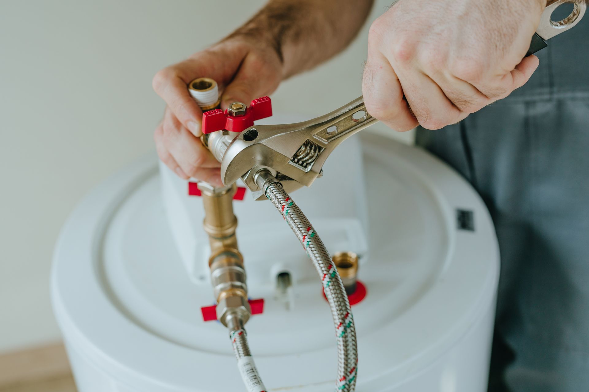 A person uses an adjustable wrench to tighten a metal hose fitting on a white water heater.