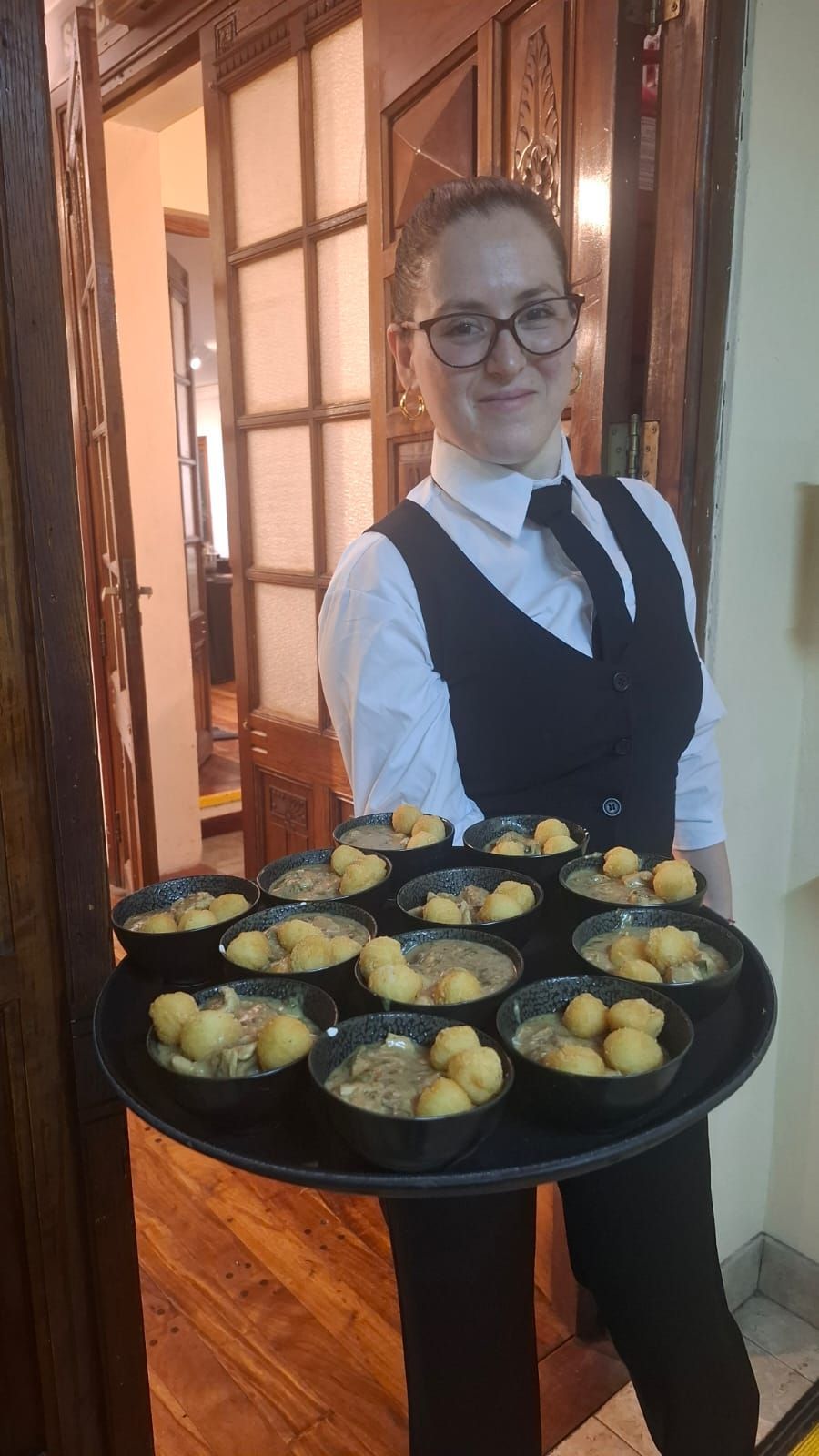 Servidor sosteniendo una bandeja con cuencos de comida; interior del restaurante.