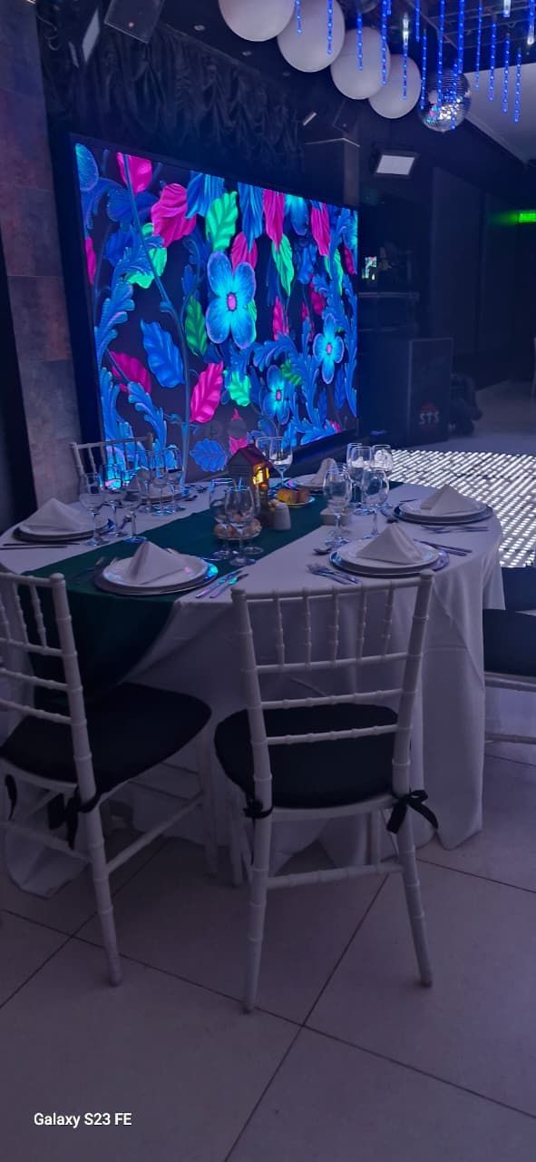 Una mesa preparada para un evento especial con una pantalla LED con estampado floral de fondo.