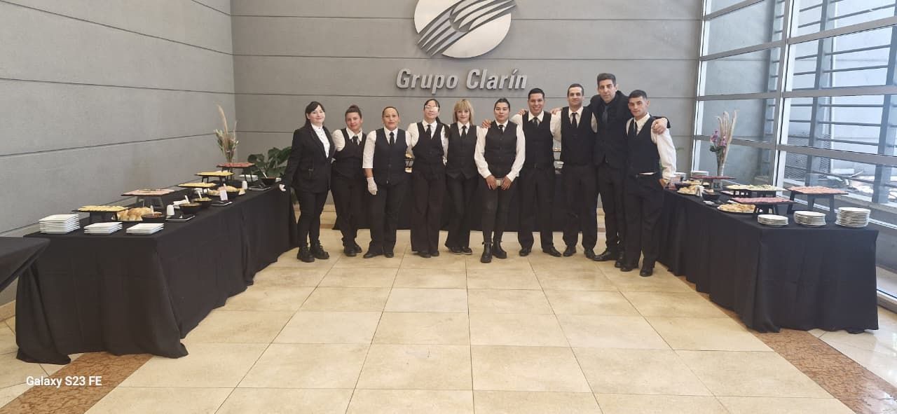 Grupo de personas uniformadas frente a mesas con comida, bajo un logo.