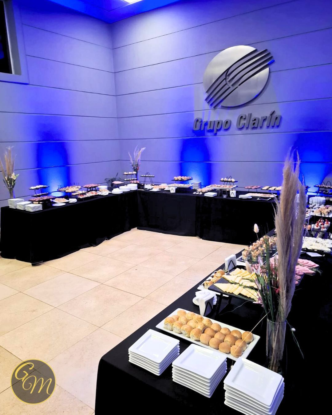 Montaje de buffet con comida sobre manteles negros, frente a una pared iluminada en azul