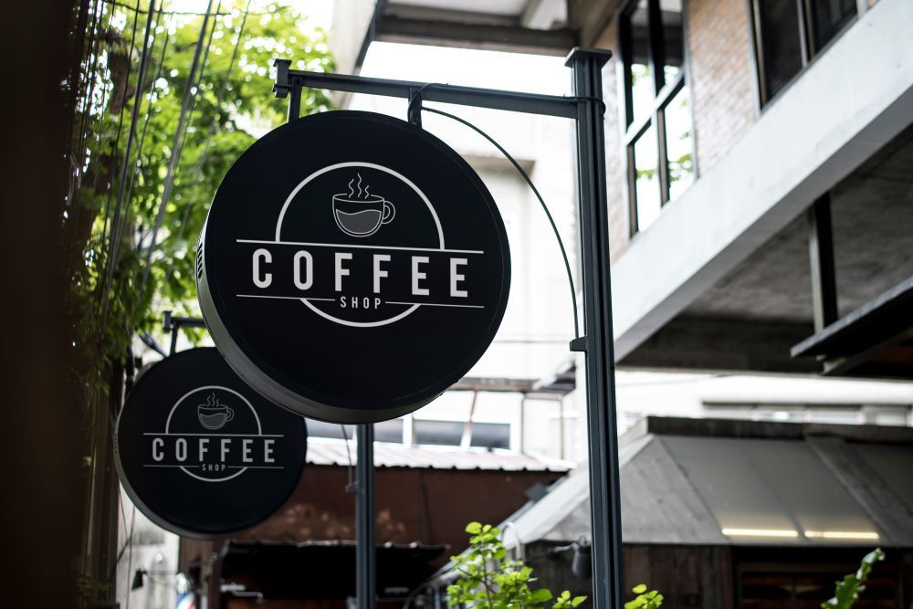 Two Signs for a Coffee Shop Are Hanging Outside of a Building — Sign Media Solutions in Ballina, NSW