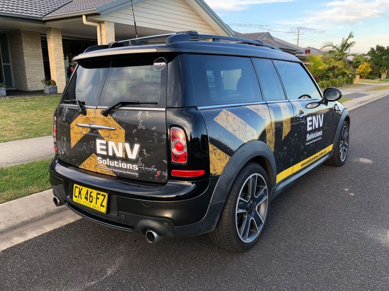 A Black Mini Cooper is Parked on the Side of the Road in Front of a House — Sign Media Solutions in Ballina, NSW