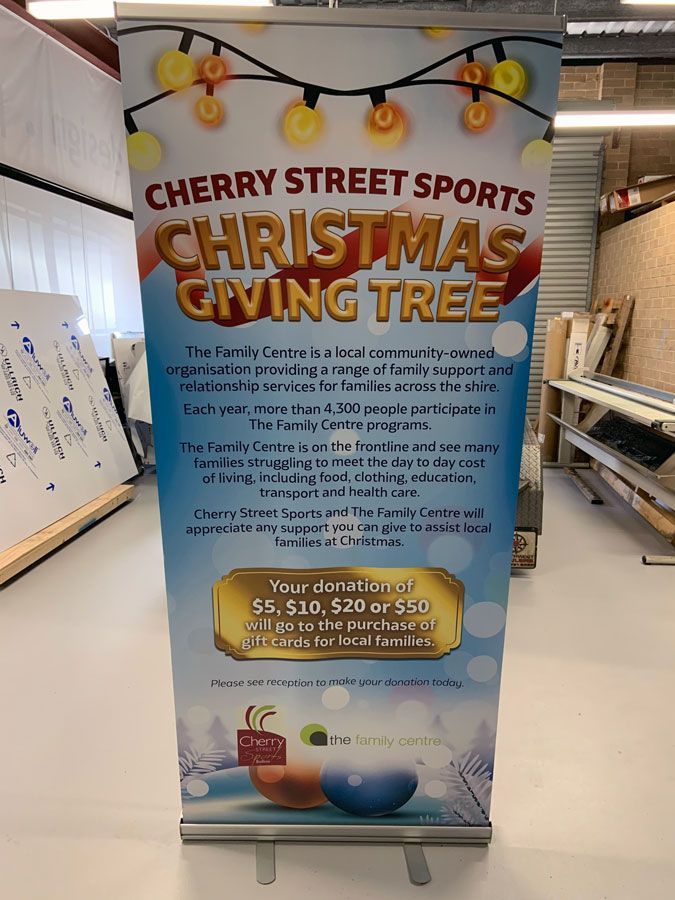 A Cherry Street Sports Christmas Giving Tree Banner is Sitting on a Table in a Room — Sign Media Solutions in Ballina, NSW