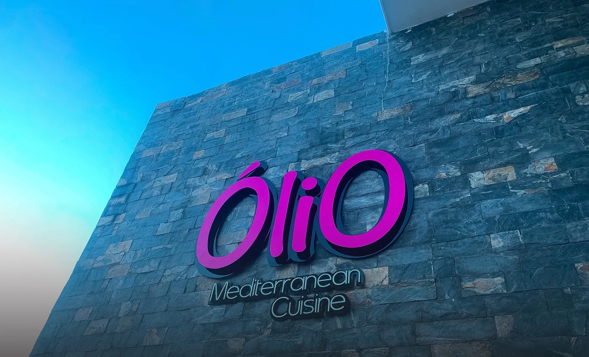 Un cartel morado en una pared de ladrillos dice Olio Cocina Mediterránea.