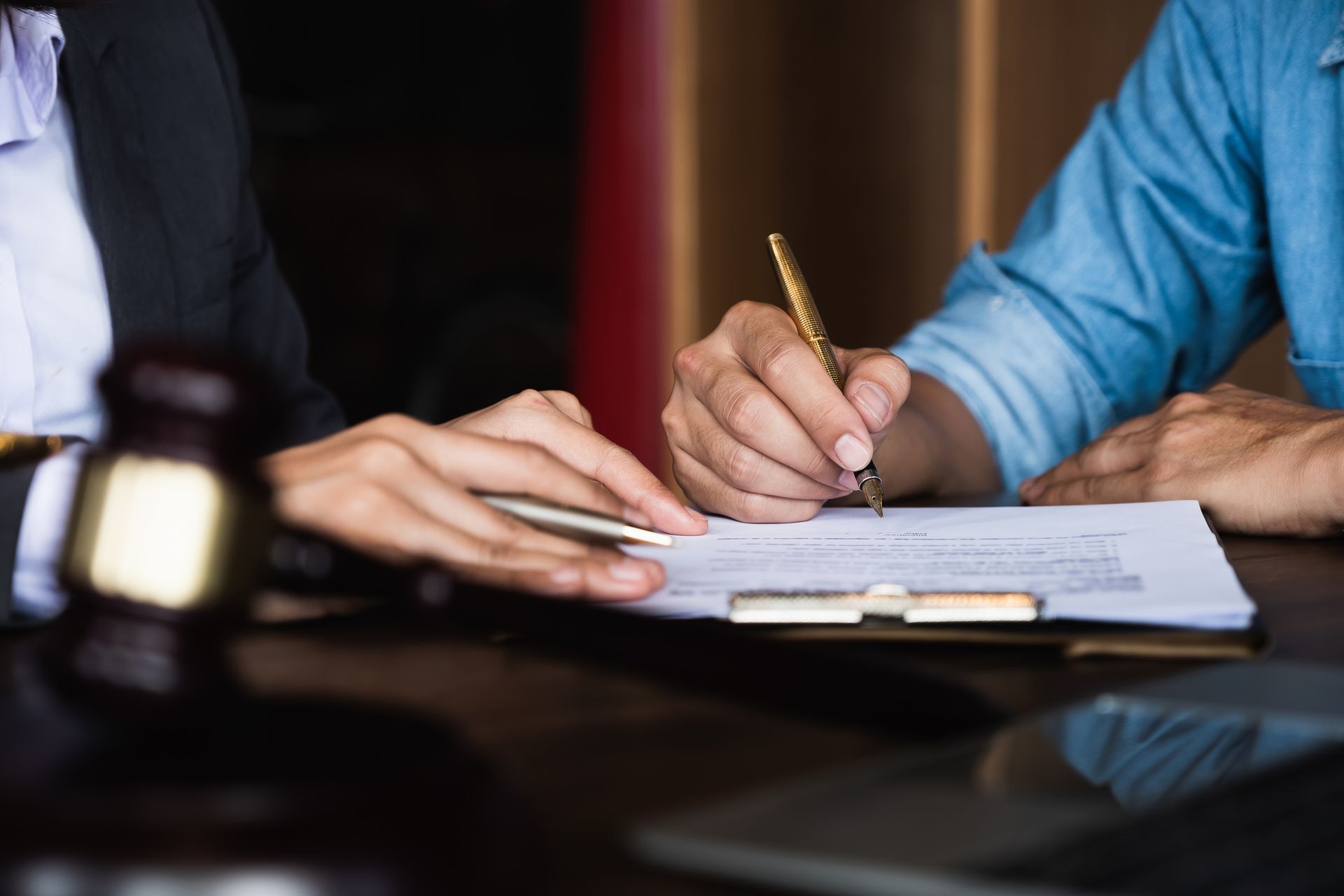 Lawyer with client reviewing paperwork, ready to sign, gavel on table.