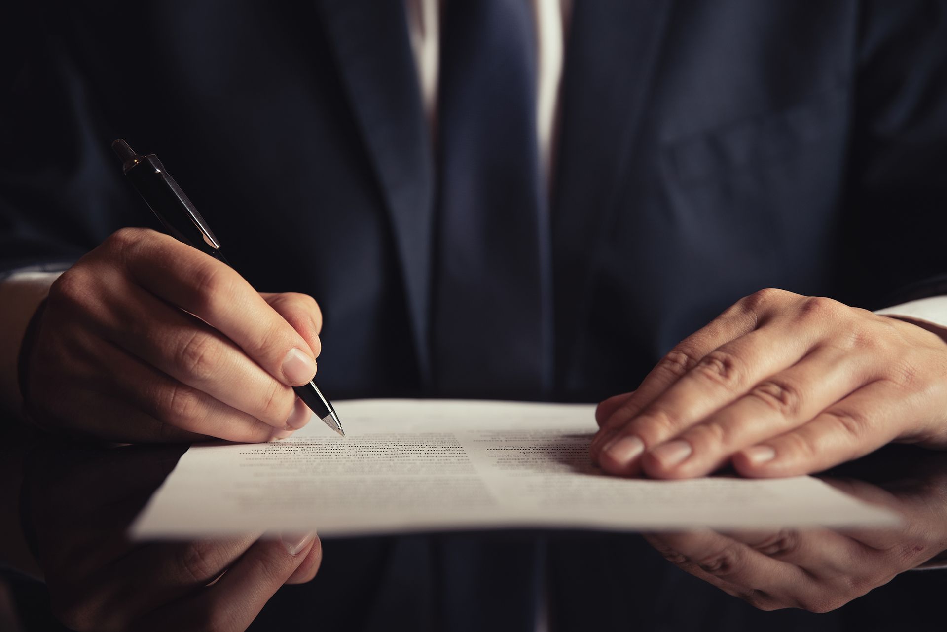 Person in a suit signing a document with a pen. Close-up on hands and paper.