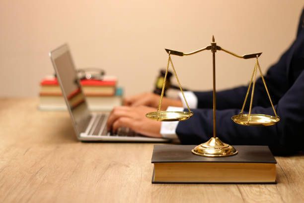A person in a suit using a laptop with scales of justice and books on a wooden desk.