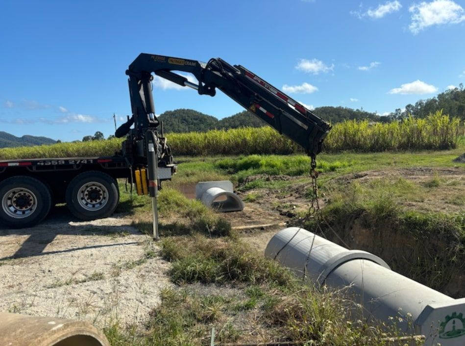 A Crane Is Lifting A Large Pipe In A Field — Single Transport Services In Moranbah, QLD