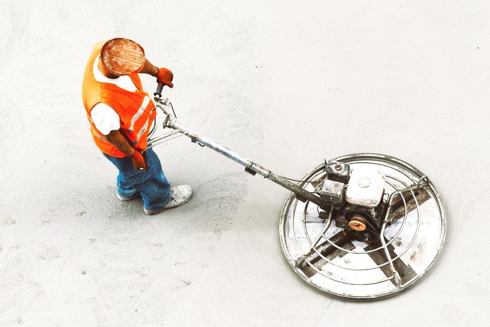 A Man in an Orange Vest is Using a Machine on a Concrete Surface — Bowen Hire & Sales in Bowen, QLD