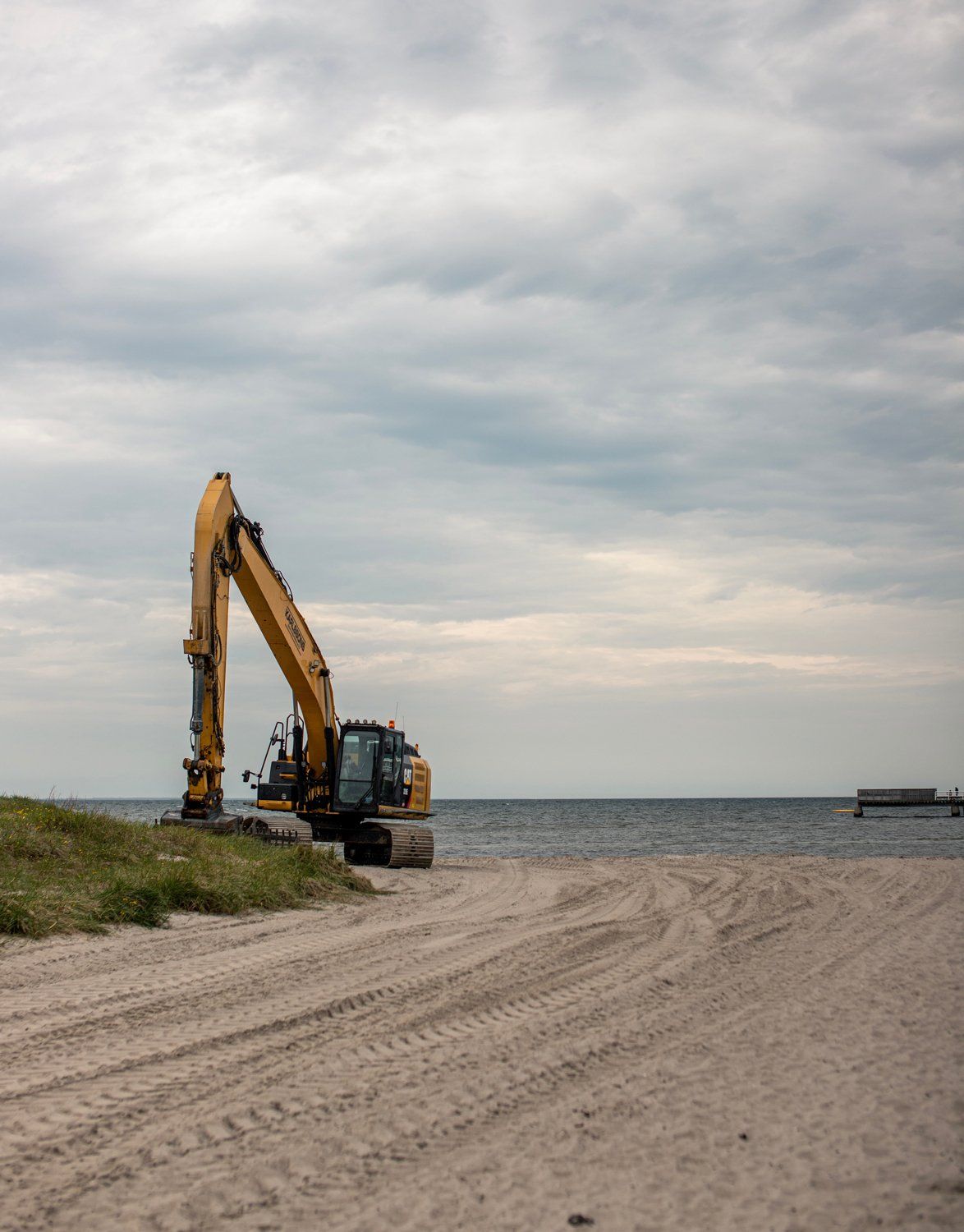 A Large Yellow Excavator is Parked on a Sandy Beach Near the Ocean — Bowen Hire & Sales in Bowen, QLD